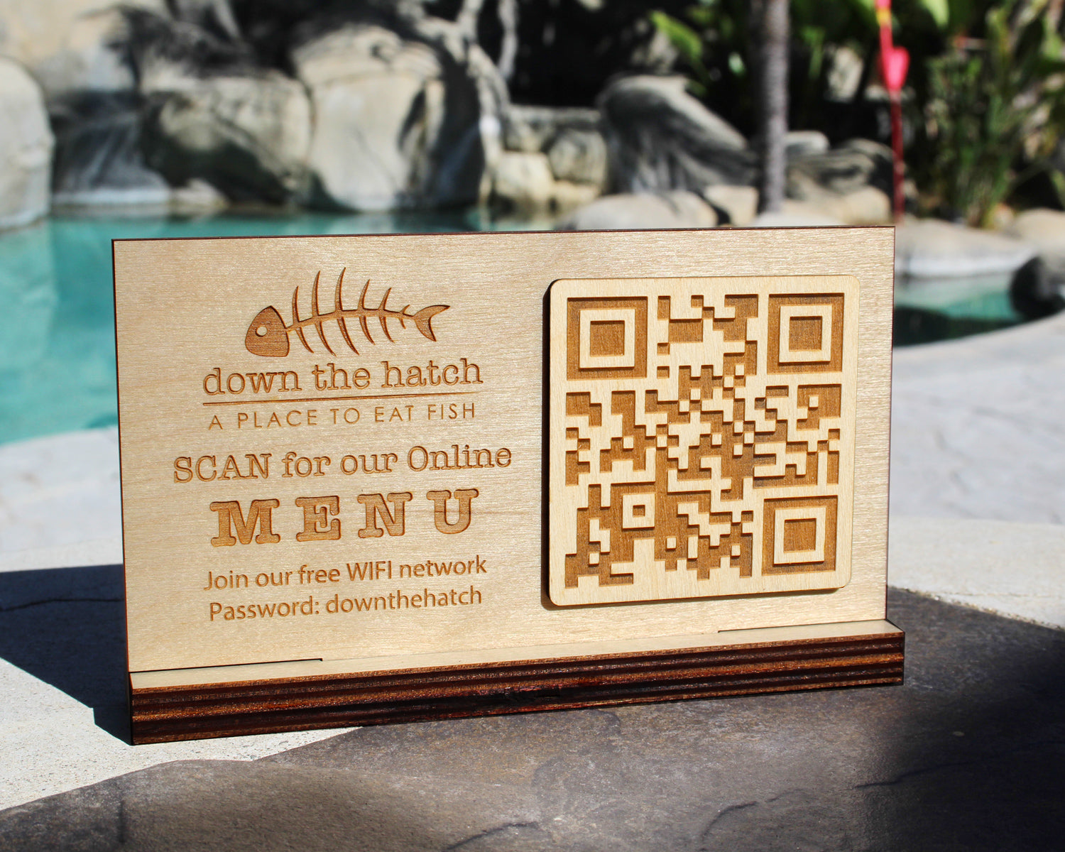 Wooden sign with QR code and text for a restaurant, placed outdoors.